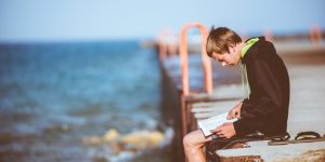 a boy sitting on a dock while reading a book