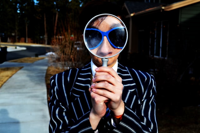 A young person with blue sunglasses holding a magnifying glass